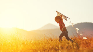 A girl running through a field with a kite at sunset