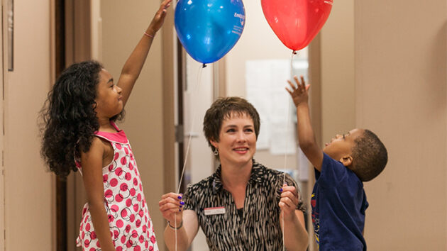 Provider gives red and white balloons to children in the hallway of a practice location.