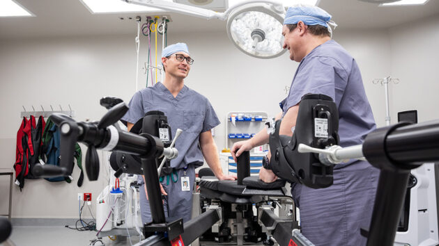 Two orthopedic surgical team members in operating room with specialized equipment.