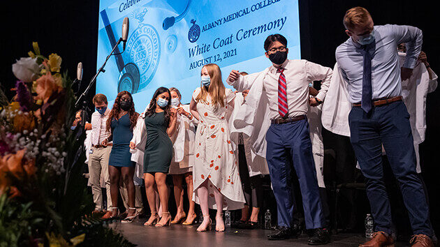 New medical students are helped into their white coats in a special "white coat" ceremony on stage. Albany Medical College classes of 2024 and 2025.