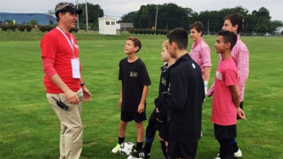 Dr. Hamish Kerr stands in a soccer field with 6 boys