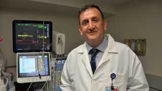 Raza Malik, MD, PhD stands next to monitoring equipment in a patient room