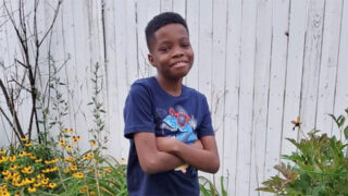 Pediatric sickle cell patient Mickoy Davis, 12, standing in his backyard by a fence