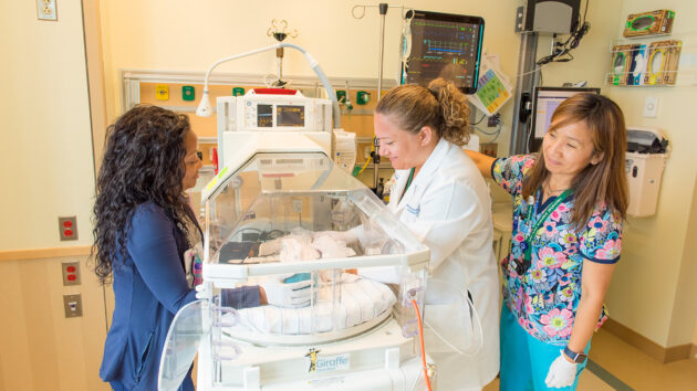 Nurses and doctors looking at a baby in an incubator in the NICU