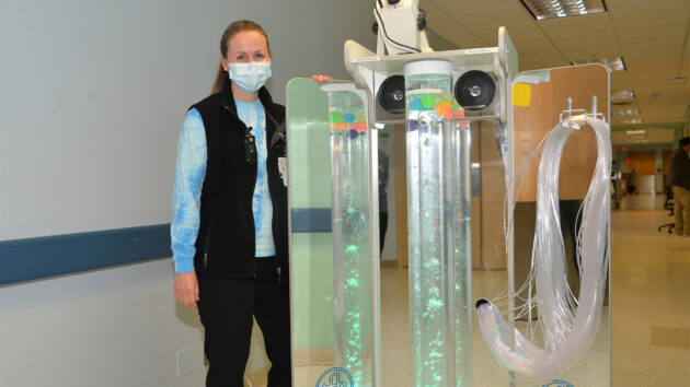 Child Life Specialist Lauren Pierce with a device to help children with autism and sensory disorders. The device is a trifold mirror with colorful bubbles and strings attached