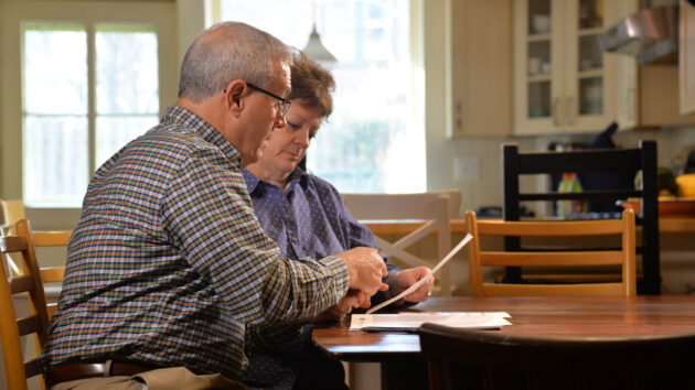 An older couple reads documents at a table in their home