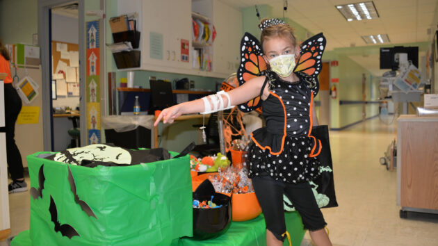 A young girl dressed as a butterfly points to Halloween supplies