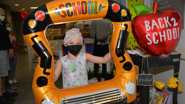 Small child wearing a face mask holding a School Bus sign during a back to school celebration at the Melodies Center