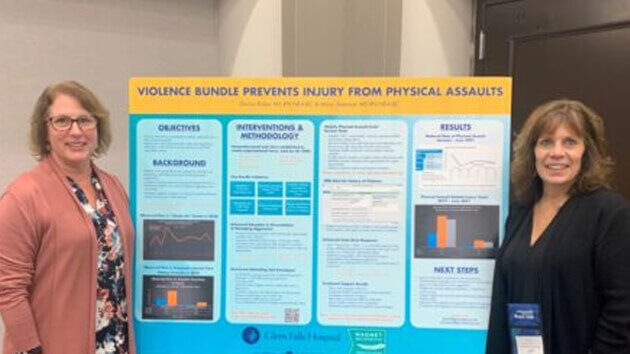 Mary Shannon, MS, RN, NEA-BC and Donna Kirker, MS, RN, NEA-BC, stand next to a poster detailing the work of the Task Force to Reduce Physical Assaults on Healthcare Workers