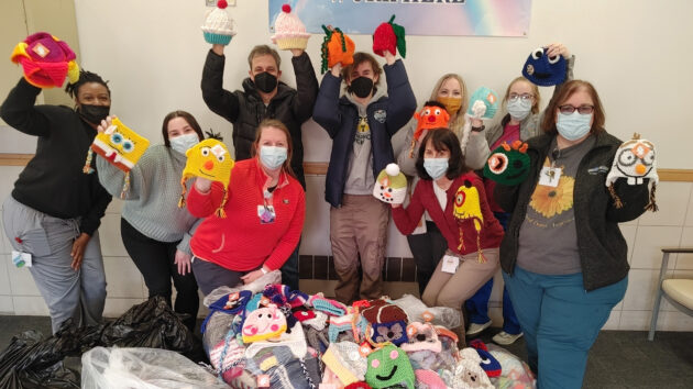 A group of people holding up colorful winter hats. Hatsgiving donated them to the Melodies Center