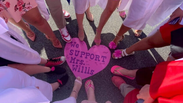 several people standing around a heart that reads "We Support Mrs. Willis" with their toes touching it