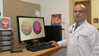 Badar Mian, MD, standing at a desk with a urological scan on the computer screen next to him.