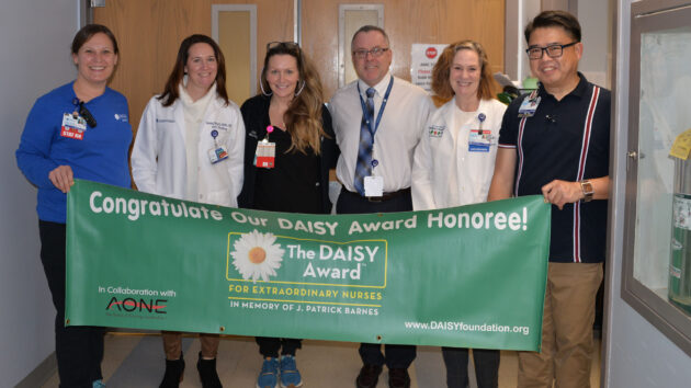 Adult STAT Nurse Micah Woodworth and team hold DAISY Award banner.