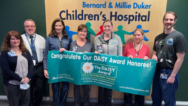 Peds STAT nurse Allie Earl and team from the Children's Hospital hold the DAISY banner.