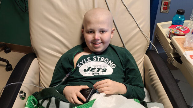 Kyle sitting in a chair wearing a NY Jets shirt that says Kyle Strong