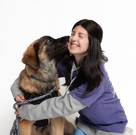 A girl hugging a service dog, that is licking her face