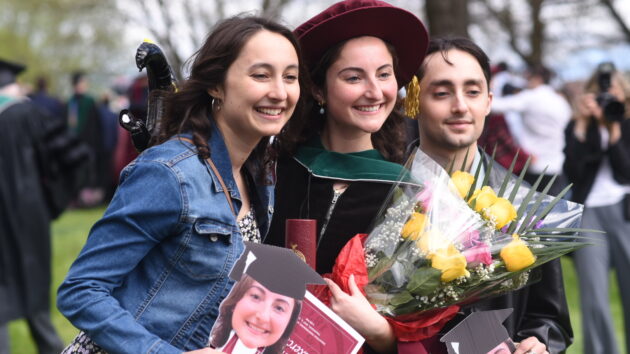 Albany Medical College Class of 2024 graduate is seen holding flowers and surrounded by friends at the Commencement ceremony