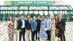 A group of people, dressed formally, stand next to the starting gate at Saratoga Race Course for the Light up the Night event