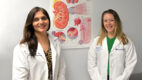 Dr. Swati Mehta, co-director, and Dr. Kelly Beers, medical director of the Glomerular Disease Center, standing in front of a poster of a kidney wearing white coats