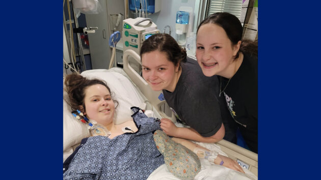 Glomerular disease patient Madison Lee in a hospital bed with her two sisters standing nearby