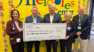 Five people standing in front of the Melodies Center sign holding an oversized check