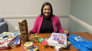 Dr. Healey sitting at a table surrounded by toys, including jenga, play doh, and board games.