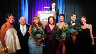 A group of people, some holding flowers, standing in front of the stage at the annual Dancing in the Woods gala.