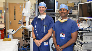 Thoracic surgeon Dr. Brian Arnold and interventional pulmonologist Dr. Nagendra Madisi standing in an operating room wearing blue scrubs