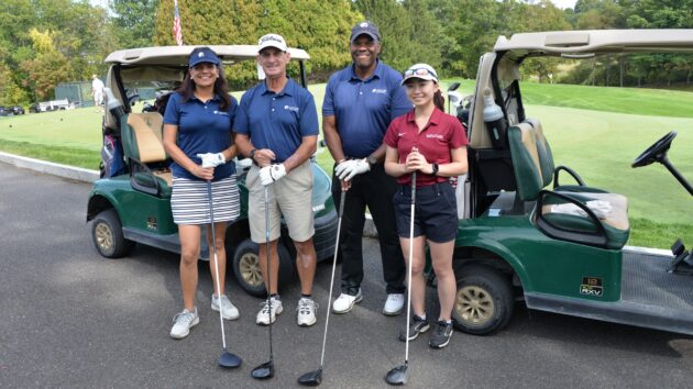 Golfers holding golf clubs, standing in front of golf carts.