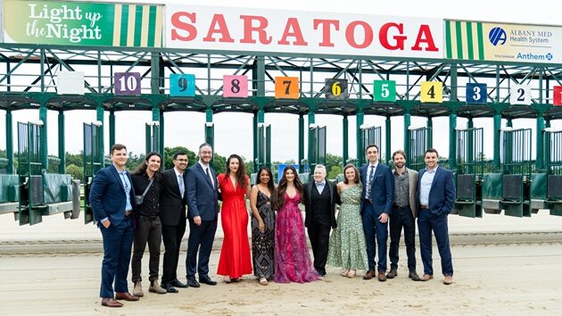 A group of people posing in front of the Saratoga Race Course starting gate at Light up the Night