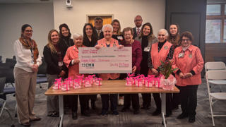 A group of hospital staff and volunteers stand behind a table while presenting a large ceremonial check for $80,000 from the Columbia Memorial Health Auxiliary.