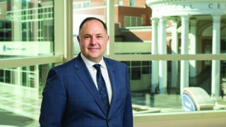 Jason Mouzakes, MD, standing on a pedestrian bridge with the Albany Medical Center pillars in the background