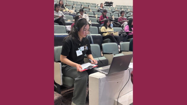 A student wearing headphones and watching a video during the practical round at the 2026 Albany Regional Brain Bee