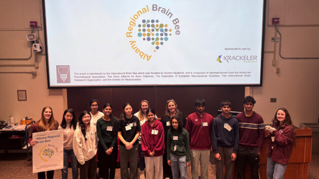 Students and committee members standing in a group at the front of a lecture hall at the 2026 Albany Regional Brain Bee