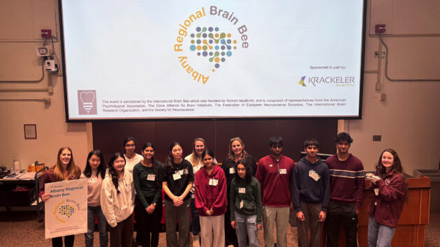 Students and committee members standing in a group at the front of a lecture hall at the 2026 Albany Regional Brain Bee
