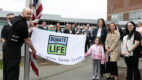 People stand alongside a Donate Life flag at a Donate Life flag raising ceremony