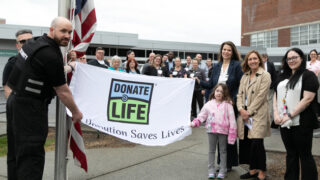 people stand alongside a Donate Life flag at a Donate Life flag raising ceremony