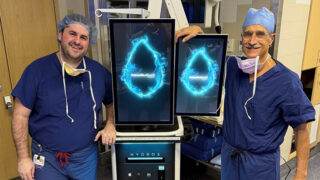 Urologists Dr. Seamus Barrett and Dr. Ronald Kaufman wearing scrubs and standing near the HYDROS Robotic System for Aquablation therapy, used to treat BPH (enlarged prostate)