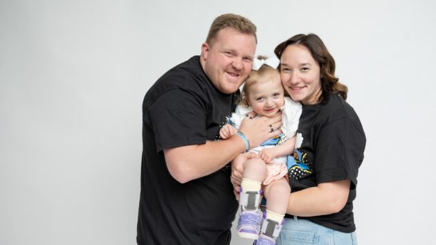 A mother and father holding their daughter between them, squeezing their cheeks against hers, as they smile for the camera.