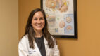 Neurosurgeon Dr. Brannan O'Neill wearing a white coat and standing in front of a poster about the brain