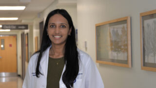 Gastroenterologist Dr. Anika Paradkar wearing a white coat standing in a clinic hallway