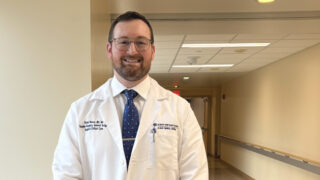 Brian Nasca, MD, standing in hospital hallway wearing white coat