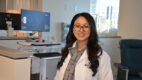 Rheumatologist Dr. Helina Maharjan wearing a white coat and standing in the infusion area of a rheumatology clinic.
