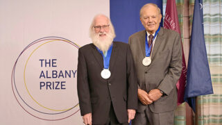 The two recipients of the 2026 Albany Medical Center Prize in Medicine and Biomedical Research standing near the Albany Prize logo wearing their Prize medals