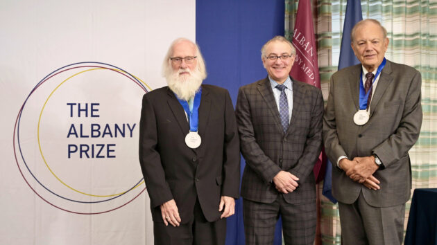 2026 Albany Prize recipients Tony Hunter, PhD, and Dennis Slamon, MD, PhD, standing by the Albany Prize logo with Albany Medical College Dean Alan Boulos, MD